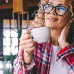 A woman drinking her coffee looking outside of her window smiling and enjoying the view