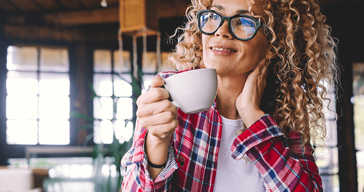 A woman drinking her coffee looking outside of her window smiling and enjoying the view